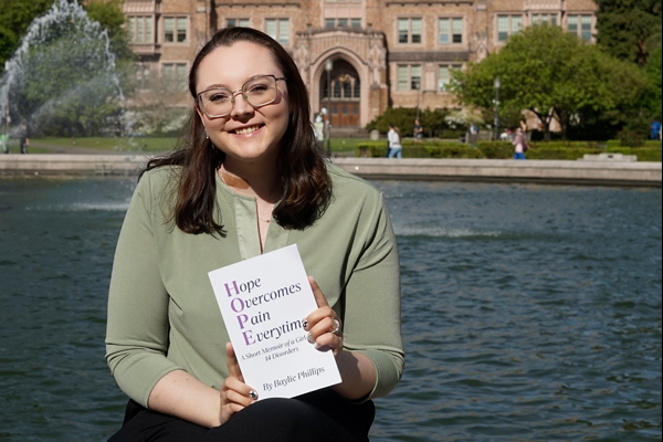 !Baylie Phillips holds her book in front of a fountain