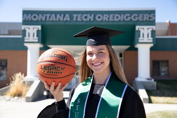 Liv in her cap and gown with a basketball outside of the HPER.