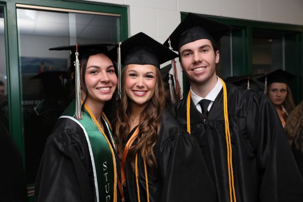 Three students pose for a photo in their cap and gown