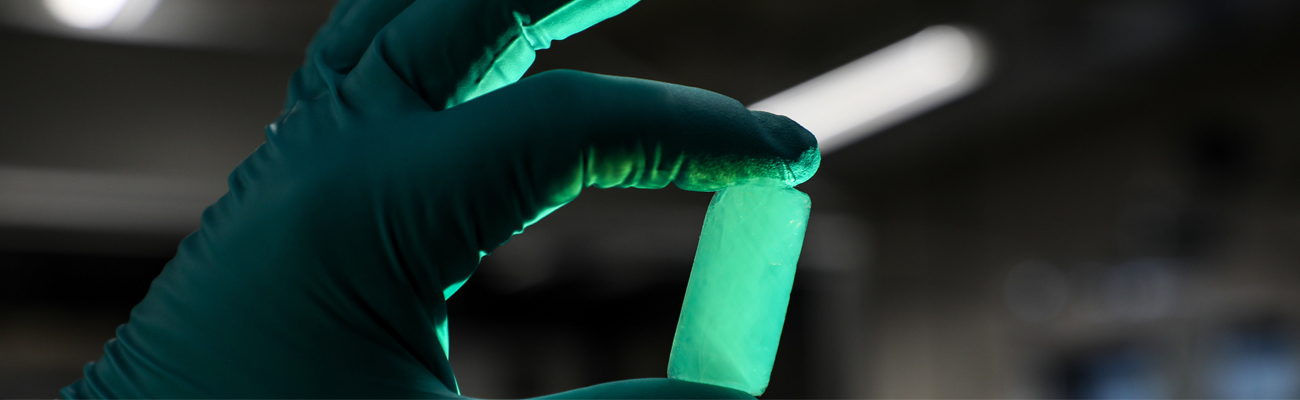 A gloved hand holds a glowing aerogel. 