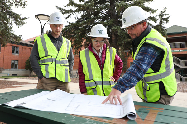 Three people wearing hi-vis vests looking at construction blueprints