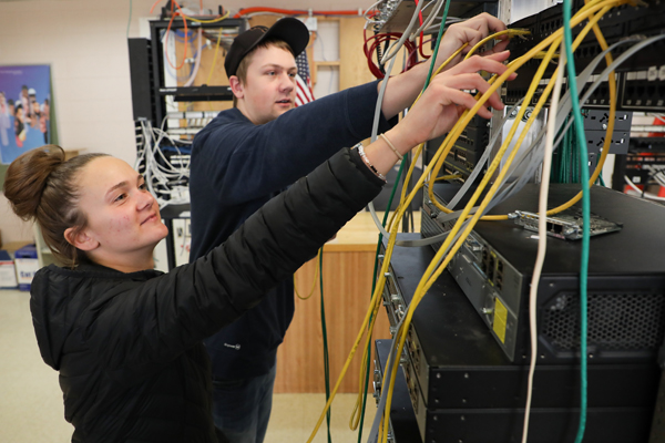 Two students plugging RJ-45 cables into a server rack.