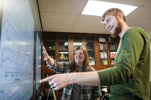 Student and staff member pointing at graphs on a smartboard