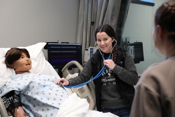 A student uses a stethoscope to listen to a mannequin.