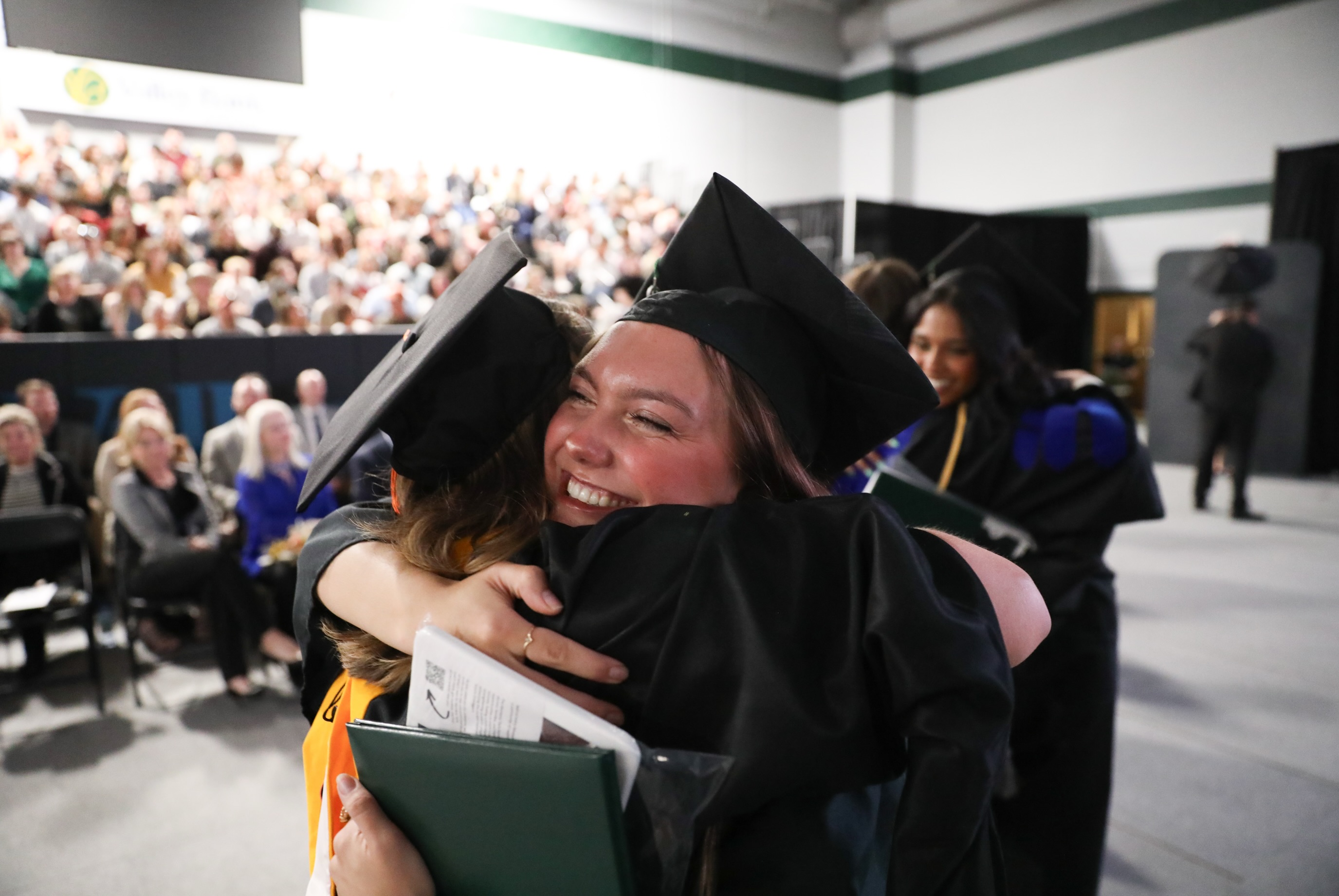 students hugging in caps and gowns 