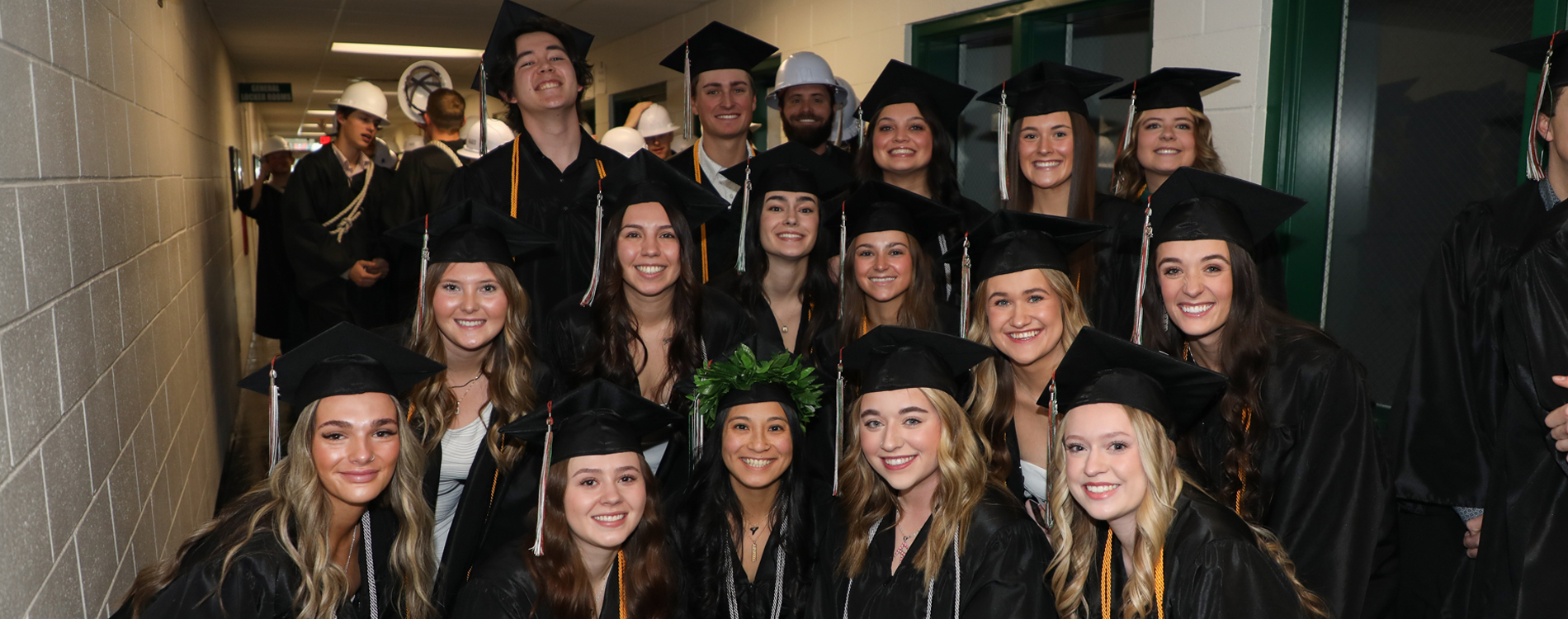 Group of smiling graduates in caps and gowns posing together in a hallway before a commencement ceremony.