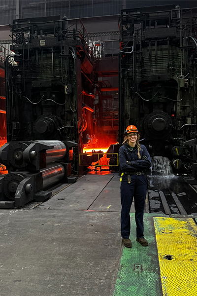 Woman wearing a hardhat in front of smelting equipment