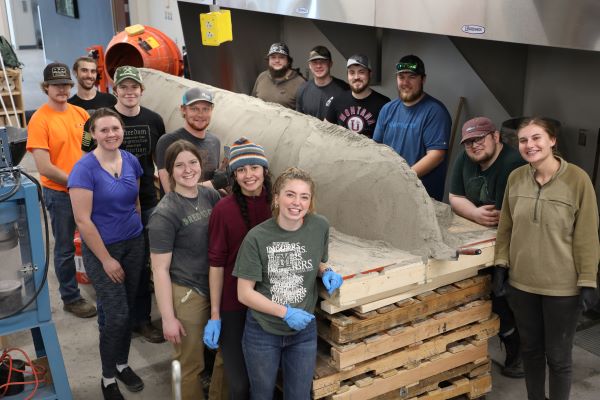 !Students stand around a concrete canoe. 