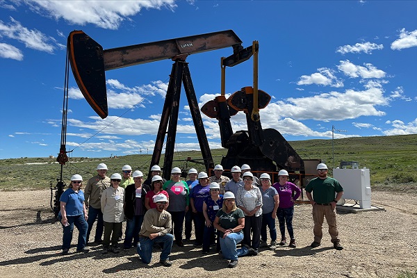 Workshop attendees stand in front of a pump jack