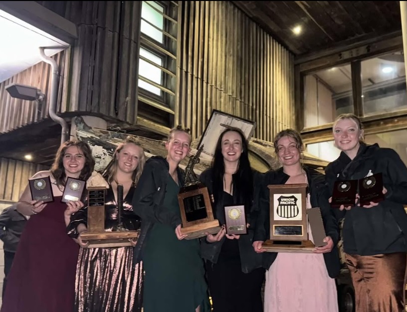 A group of female students pose with multiple trophies 