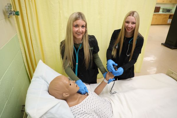 Two students smile as they work with a dummy