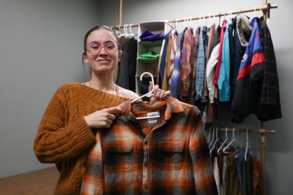 Cheyenne Crocker holds up a plaid shirt in front of clothing racks