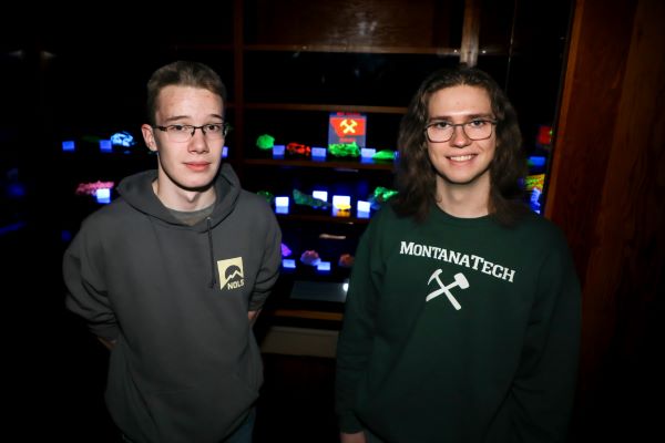 Two students in front of rocks that glow in a dark room