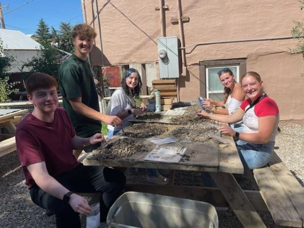 !Student appear to be digging through rocks at a picnic table as part of the summer bridge program. 