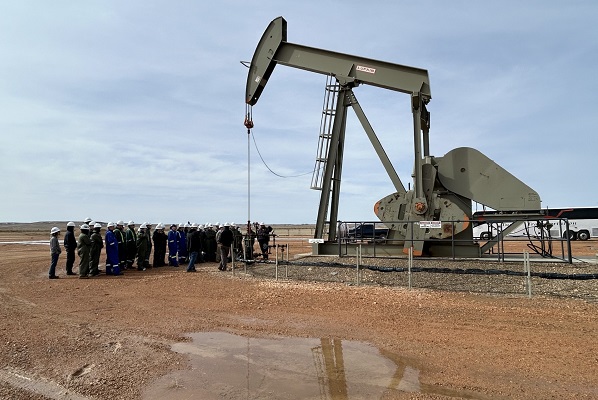 A group of students stand in front of a pumpjack. 